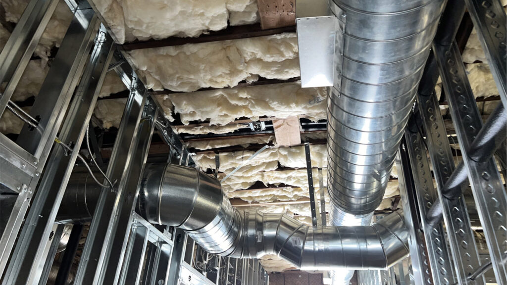 Interior view of a home under construction with exposed insulation between the framing, featuring ductwork and wiring, emphasizing the importance of insulation in building practices.