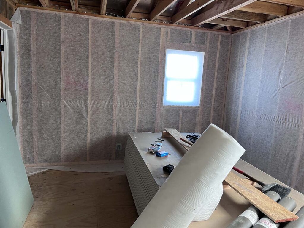 A construction site showing walls lined with new fiberglass insulation, ready for drywall installation, showcasing steps toward energy-efficient building.