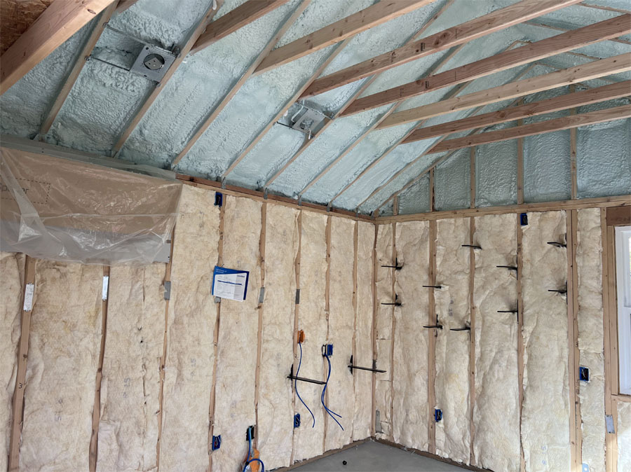 Interior of a construction site with exposed beams and fiberglass insulation in the process of being installed on the walls and ceiling.