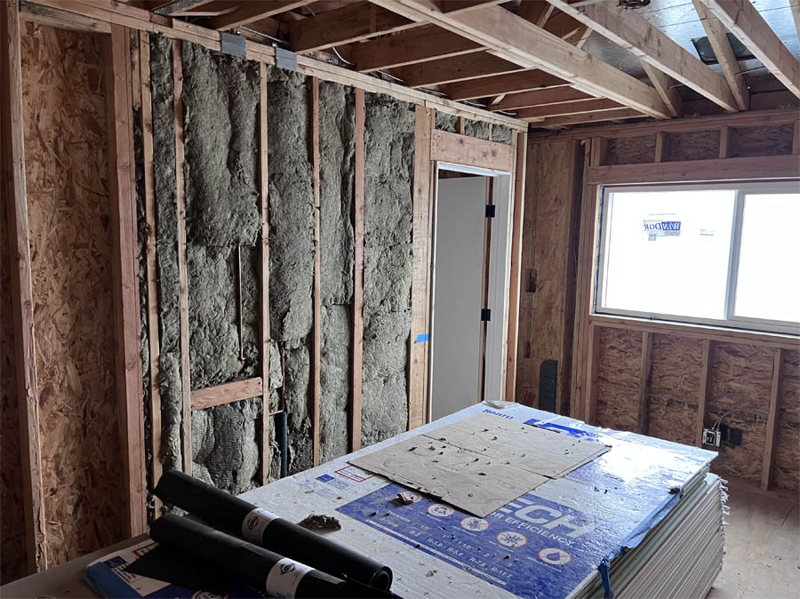 An unfinished room with exposed wooden studs filled with thick green insulation material, with a window and door framing visible, highlighting the installation process.